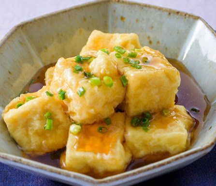 Tofu cubes in sauce garnished with chopped green onions in a small bowl