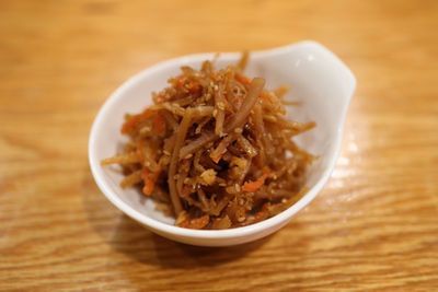 Small white dish of shredded brown pickled vegetables on a wooden table
