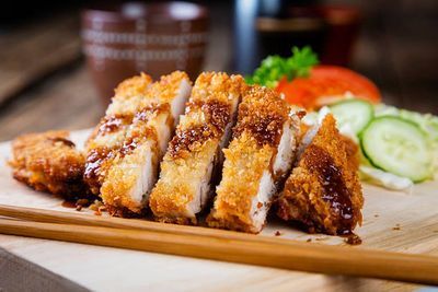 Breaded fried cutlet slices on a wooden board with cucumber and tomato garnish