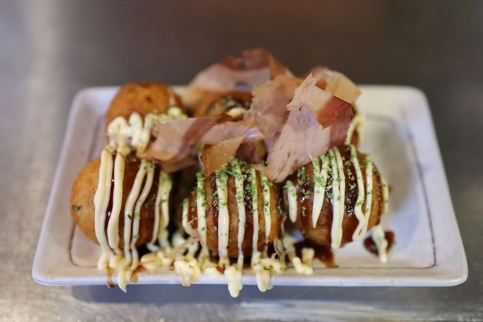 Tray of loaded hot dogs topped with sauces, herbs, and bacon bits