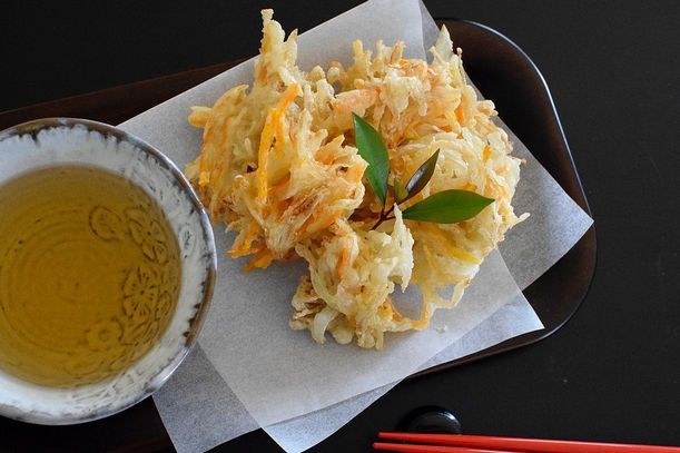 Tempura dish with dipping sauce on a black tray, served with red chopsticks