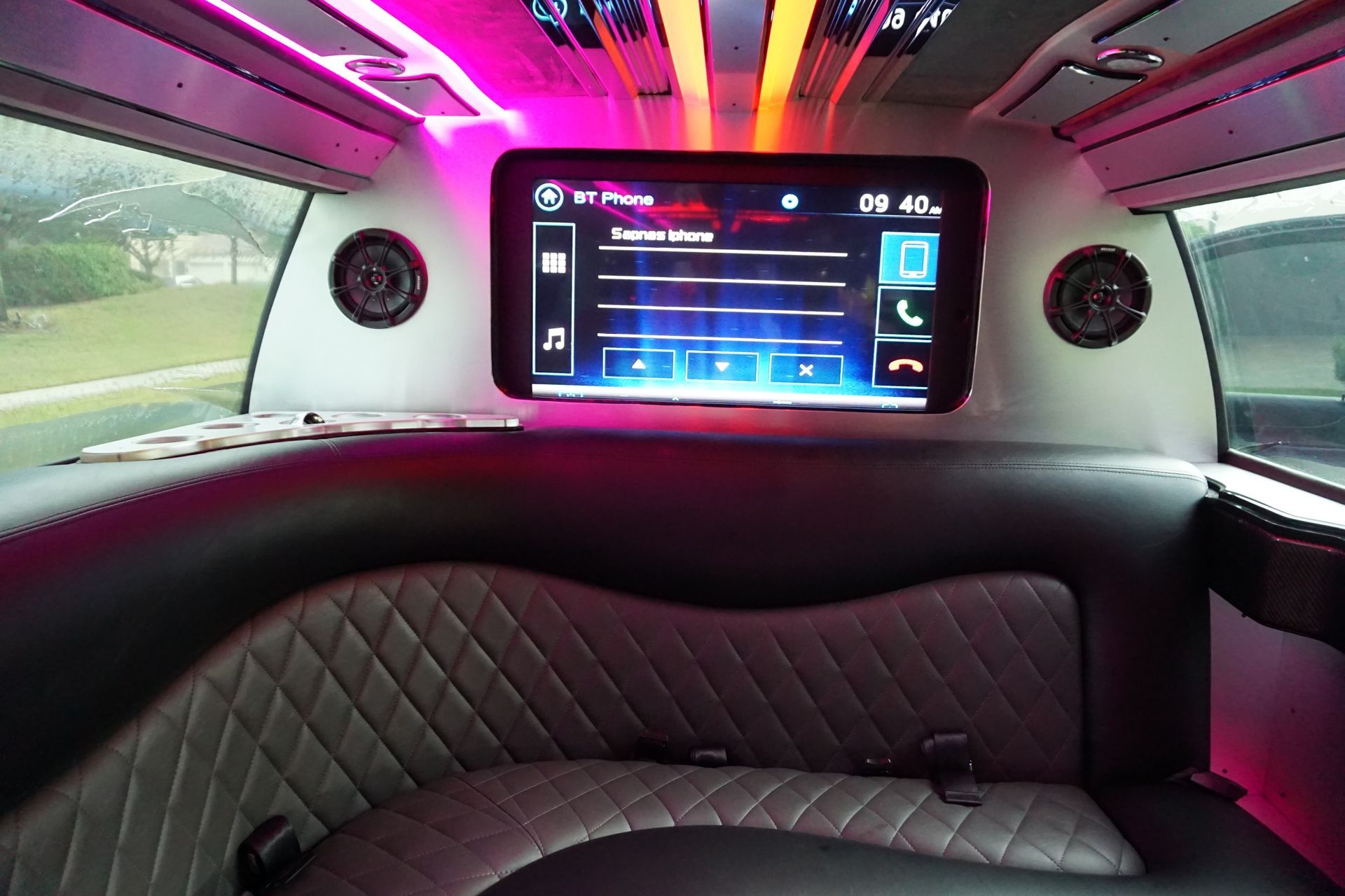 Interior of a luxury limo with diamond-stitched gray seating, ambient pink lighting, and a centrally mounted touchscreen.