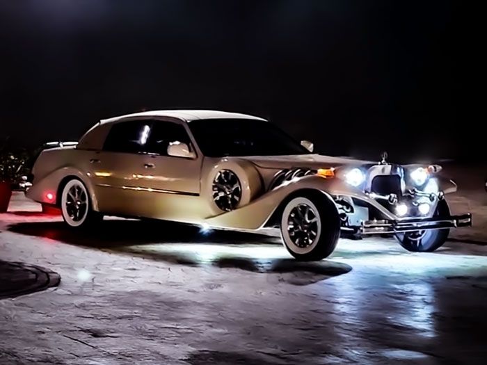 A cream-colored, vintage-style Zimmer Golden Spirit car parked at night with bright, illuminated headlights.