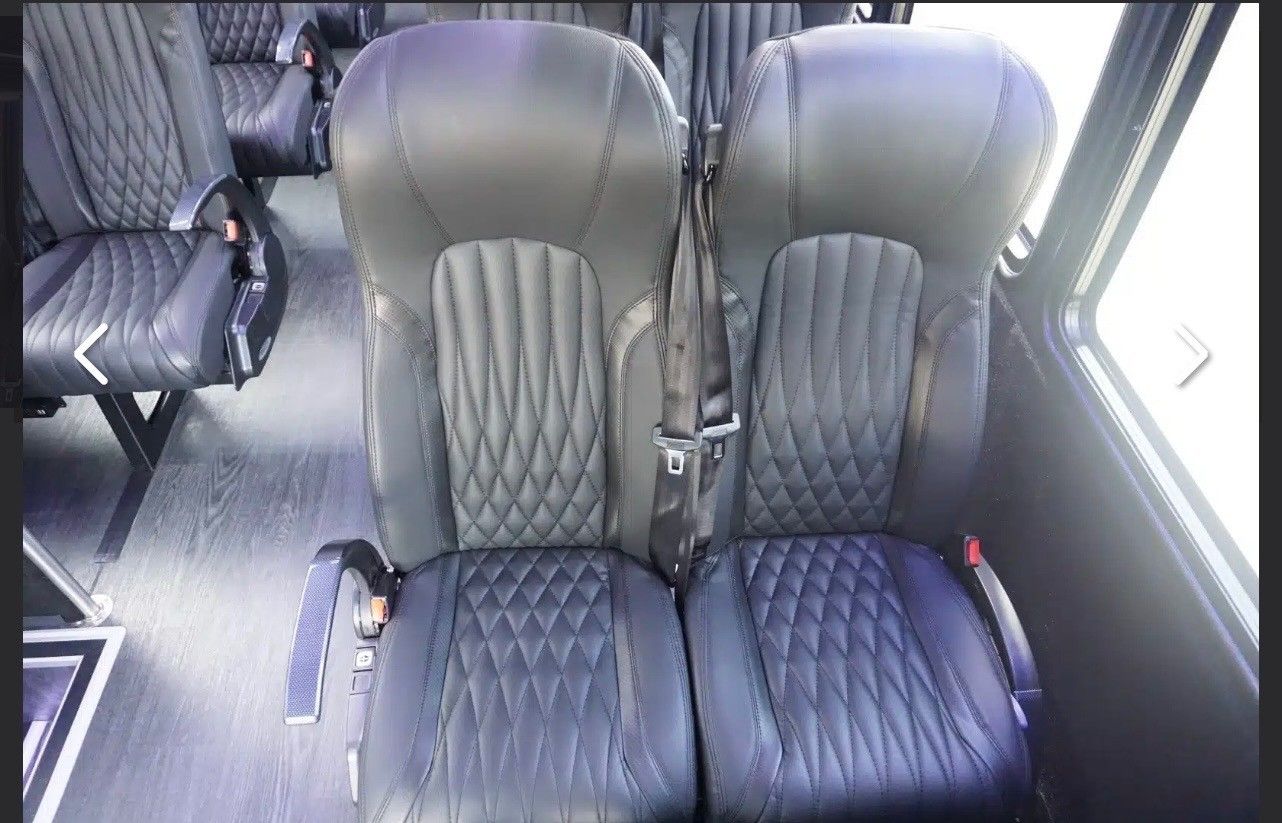 Rows of black, diamond-stitched leather passenger seats inside a vehicle with grey flooring and large side windows.