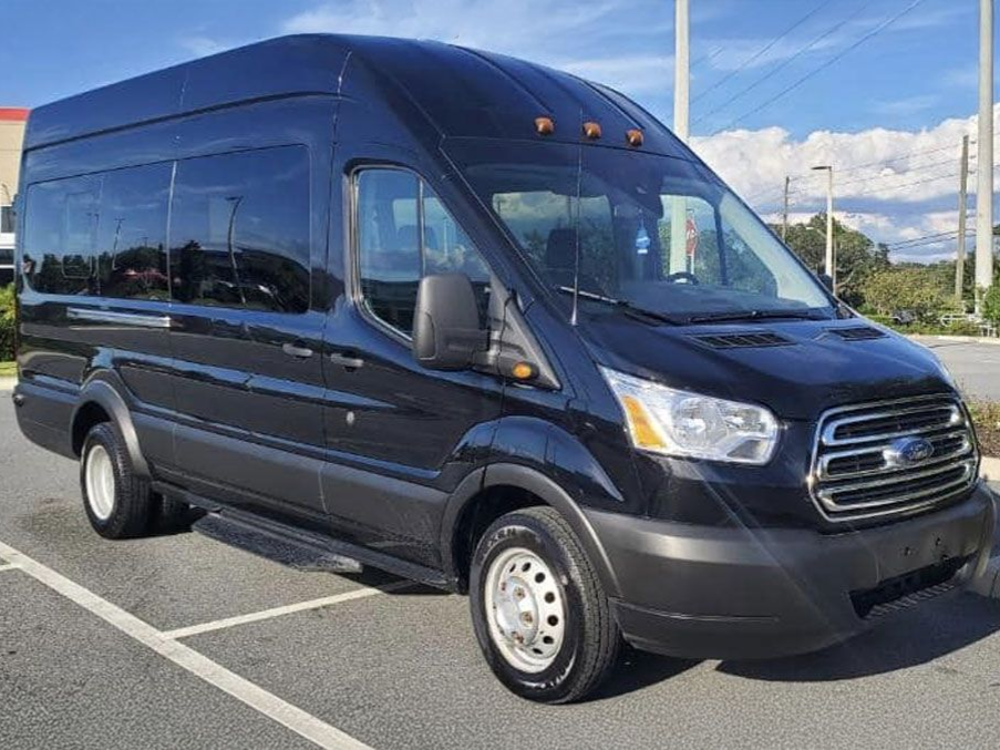 A black Ford Transit high-roof passenger van parked in a parking lot under a sunny sky.
