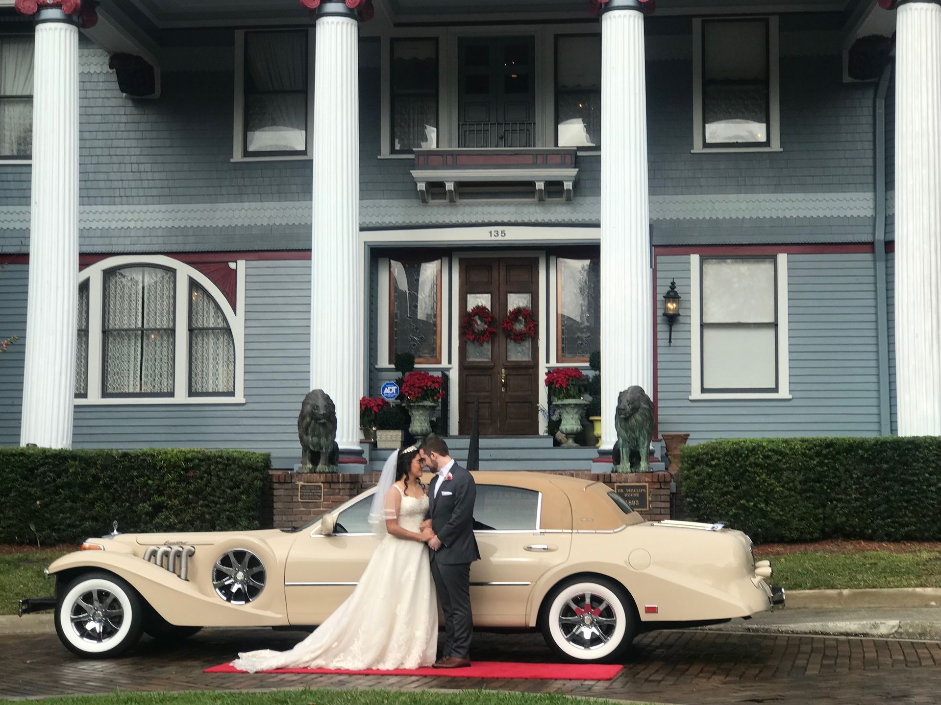 Exotic Limo Orlando Couple embraces beside a beige convertible in front of a blue mansion with white columns
