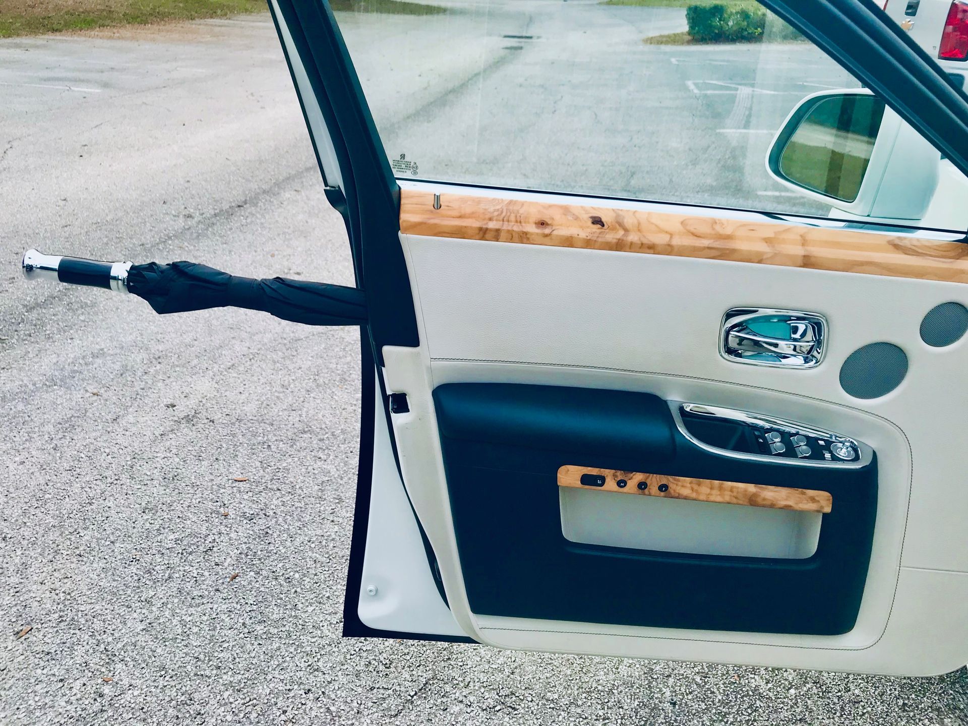The inside of a luxury car door with a black umbrella stored in a built-in slot, featuring cream leather and wood trim.