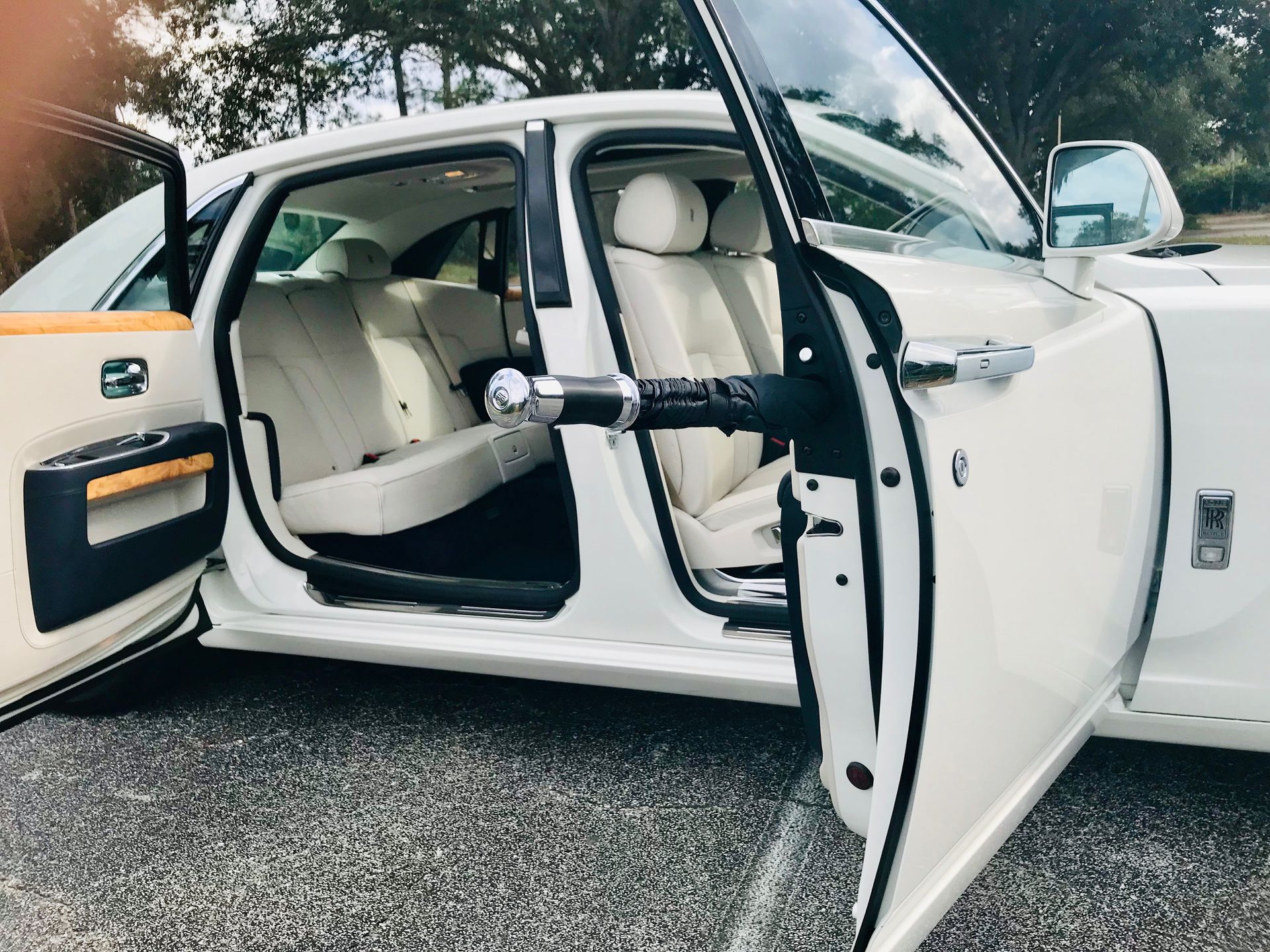 A white Rolls-Royce with its rear-hinged coach doors open, revealing a luxurious interior with cream-colored leather seats.
