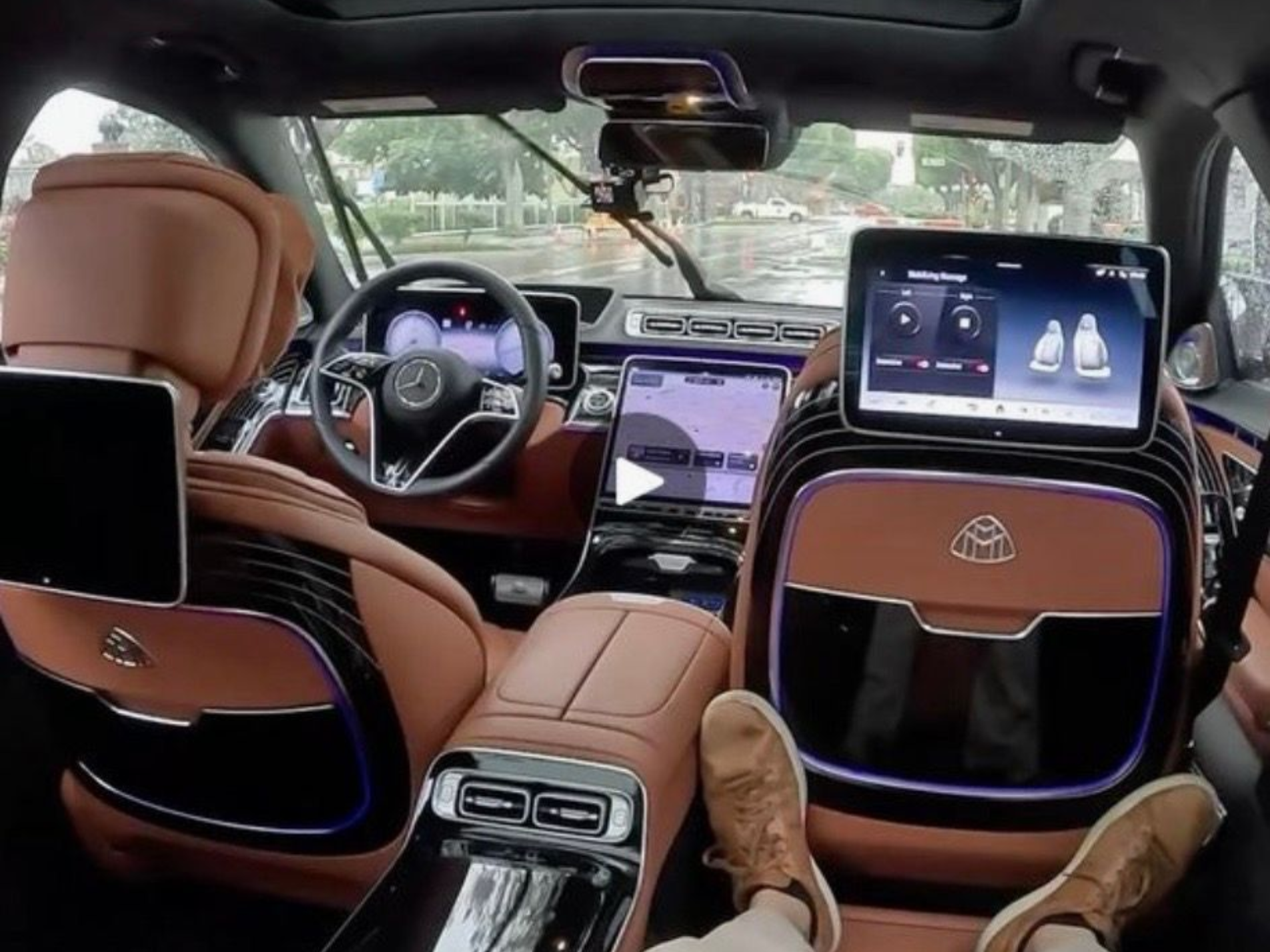 The interior of a luxury Maybach, featuring brown leather seats, rear-seat entertainment screens, and a view of the road.