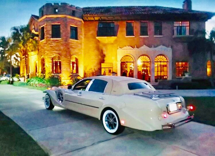 Excalibur Godfather parked in front of a large mansion at dusk, lit by warm lights.Exotic Limo Orlando