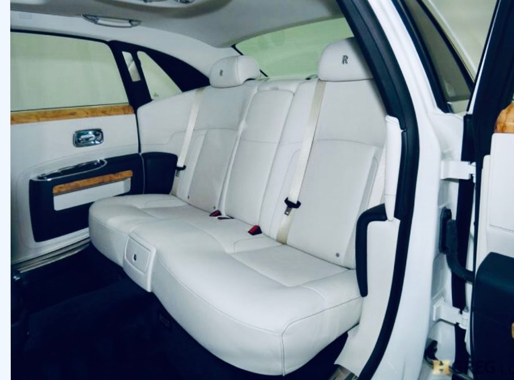 The interior back seat of a luxury vehicle featuring white leather upholstery, wood trim, and a high-end design.