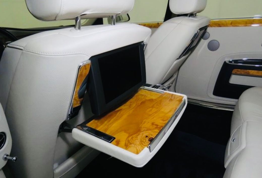 A car seat back with a deployed wooden tray table and an integrated entertainment screen in a light-colored interior.