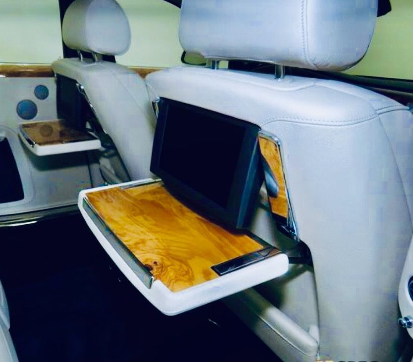 The interior of a luxury vehicle featuring light leather seats with integrated wooden tray tables and rear-seat monitors.
