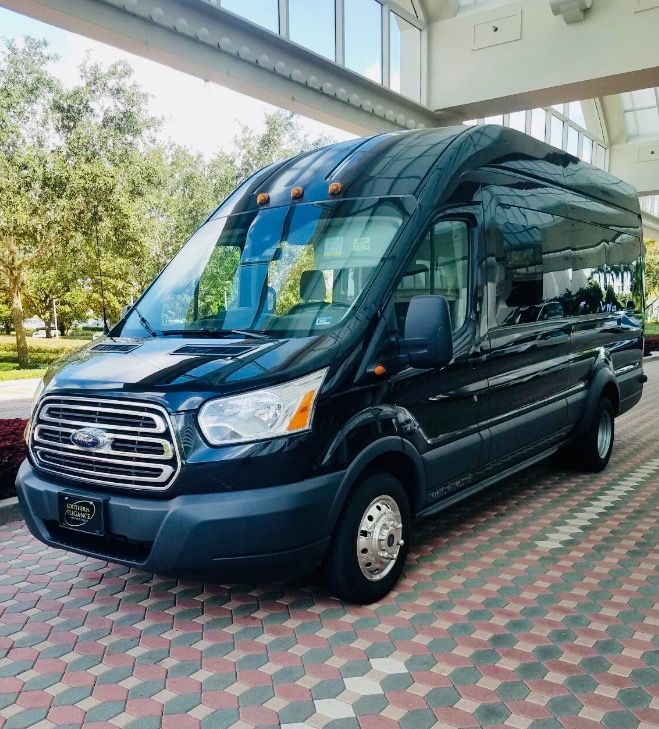A black Ford Transit high-roof passenger van parked on a paved outdoor walkway.
