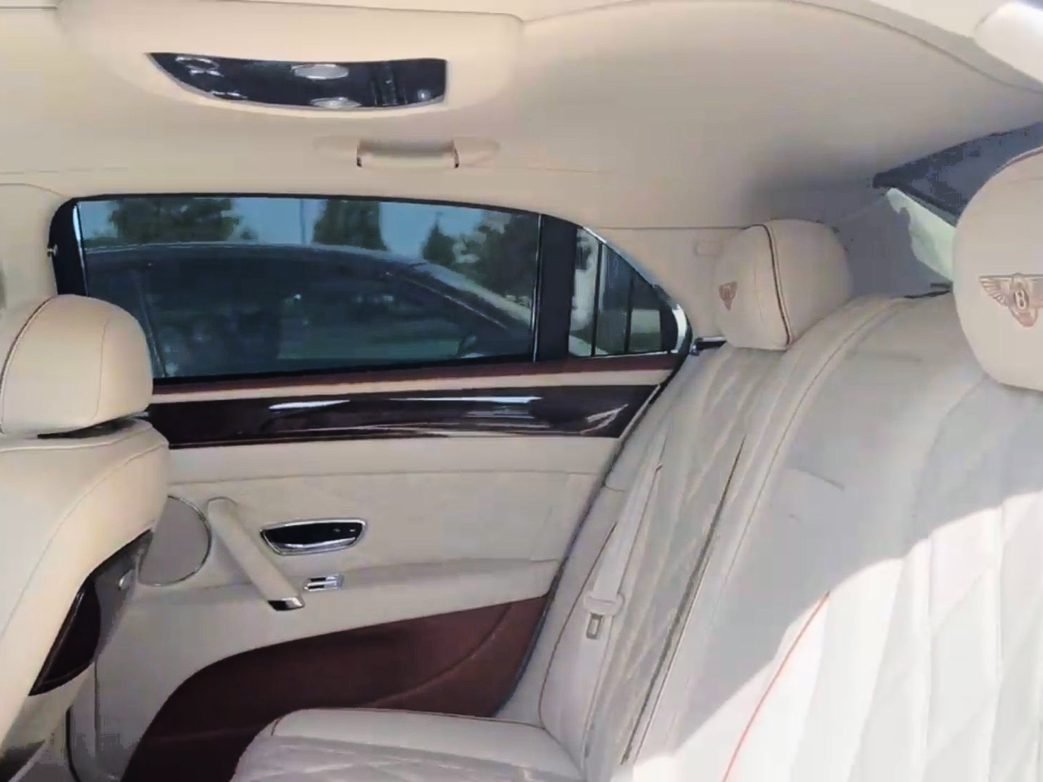 The interior of a luxury vehicle showing beige leather back seats, wood trim, and a branded headrest.