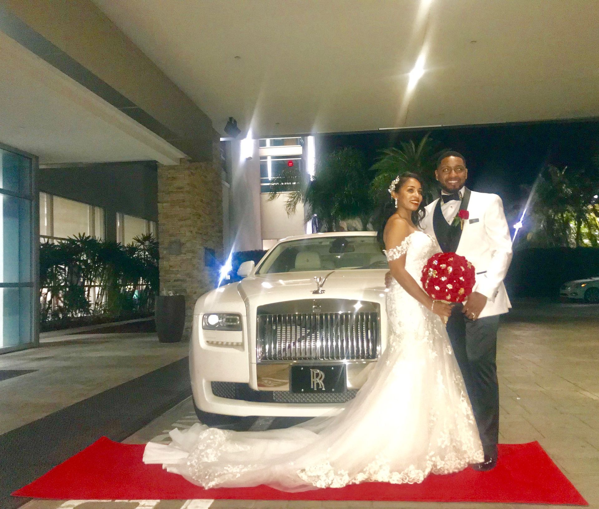 Newlyweds posing next to a white Rolls Royce on a red carpet at night.Exotic Limo Orlando