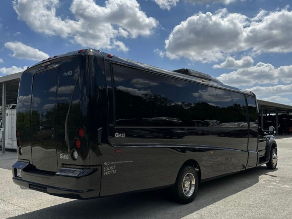 A black luxury shuttle bus parked outdoors on a sunny day with a blue sky and scattered clouds in the background.
