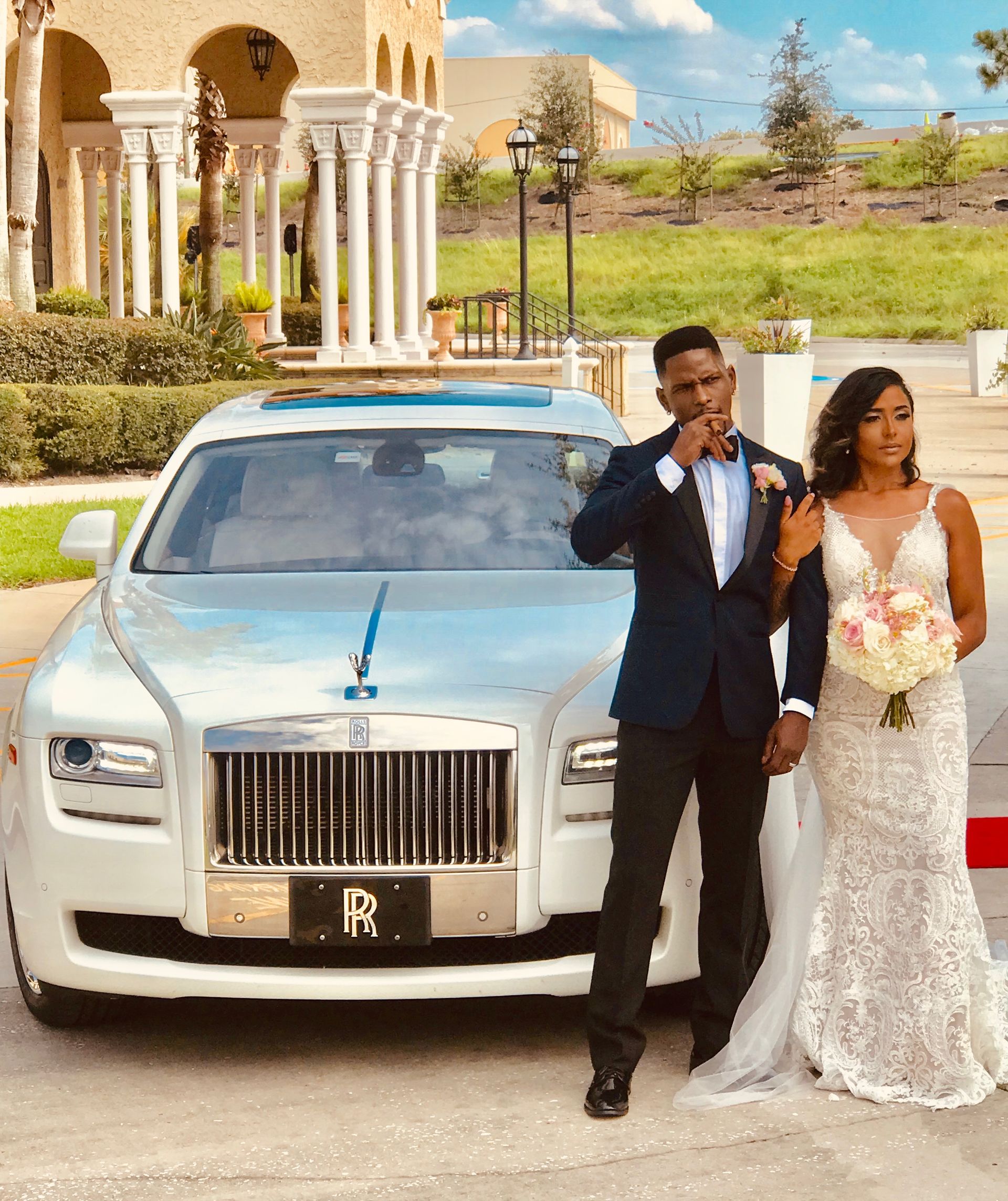 Newlyweds posing next to a white Rolls Royce. The groom wears a suit, and the bride holds a bouquet,Exotic Limo Orlando