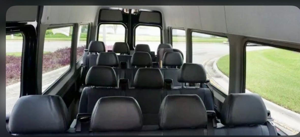 Interior view of a passenger van with rows of empty black leather seats facing toward the rear doors.