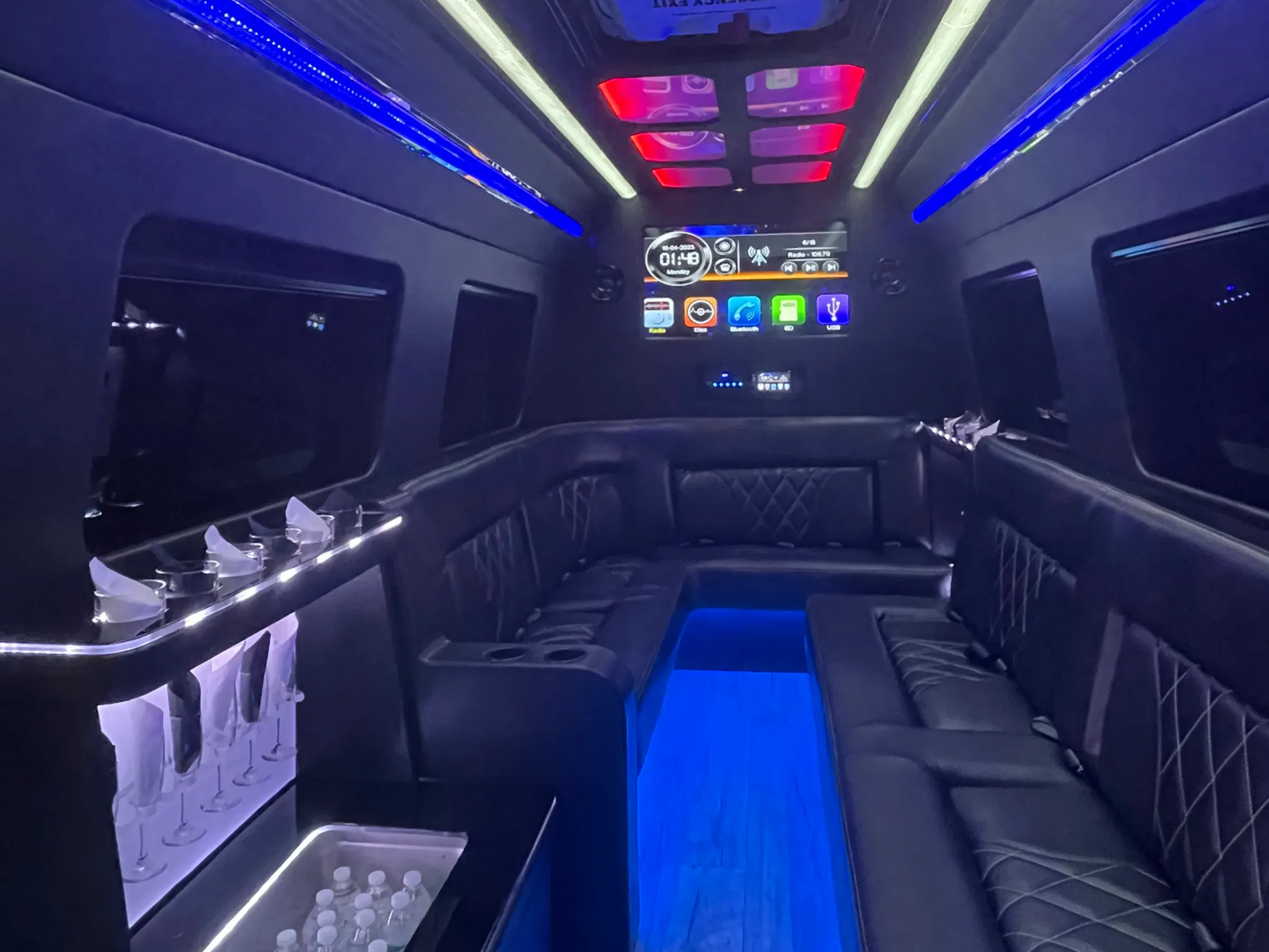 Interior of a black luxury van with blue and red accent lighting, leather seating, and a bar.