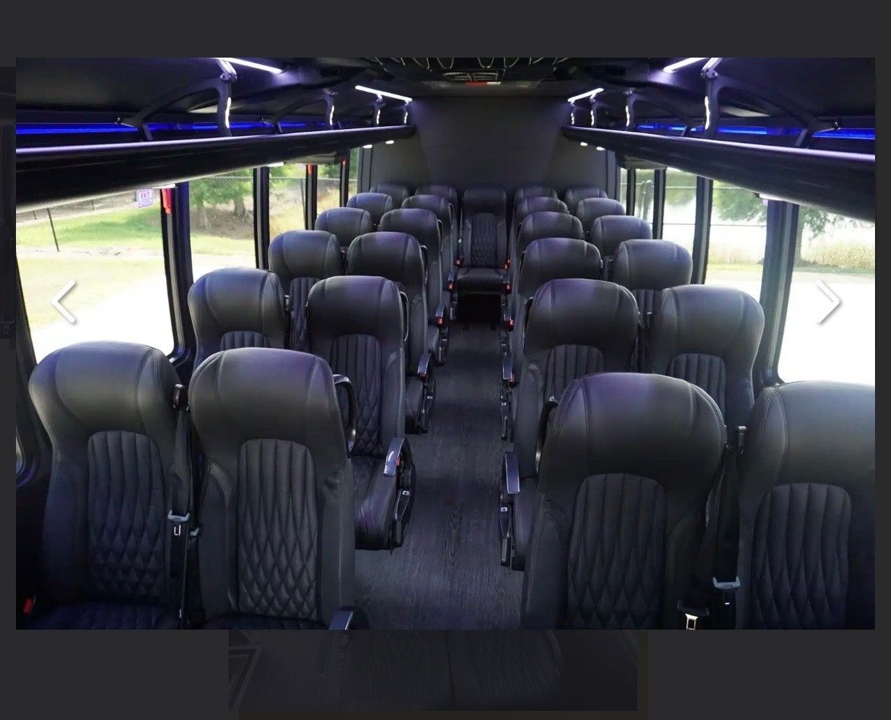 Empty interior of a bus with rows of black leather passenger seats, a center aisle, and blue overhead accent lighting.