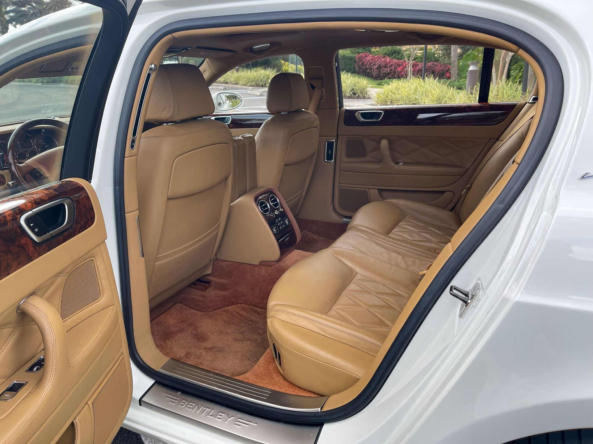 Interior of a white luxury car, featuring tan leather seats, wood-trim door panels, and plush brown carpeting.