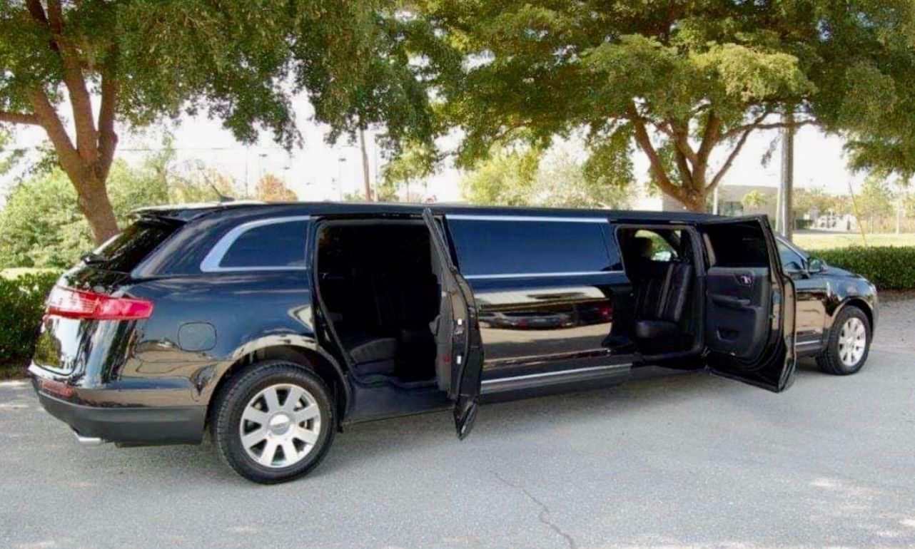 A black stretch limousine parked outdoors with its side doors open, showcasing the interior seating.