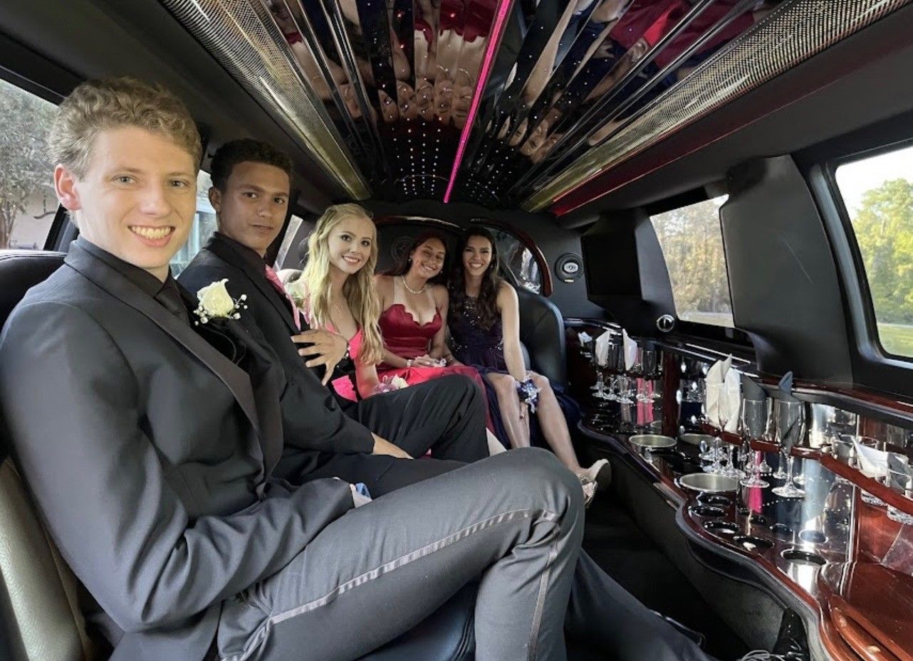 A group of five friends in formal wear riding inside a limousine with mirrored ceilings and interior bar lighting.