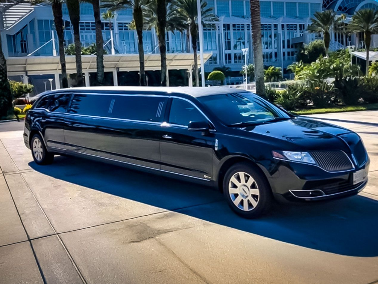 Black Lincoln limousine parked on a paved surface near a building and palm trees.