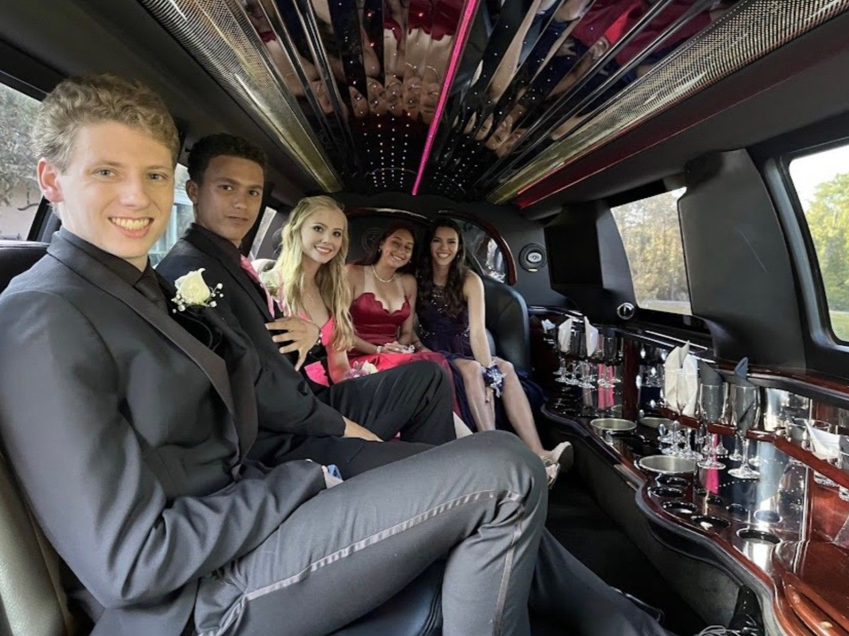 Five people in formal attire sit inside a limousine, smiling toward the camera.