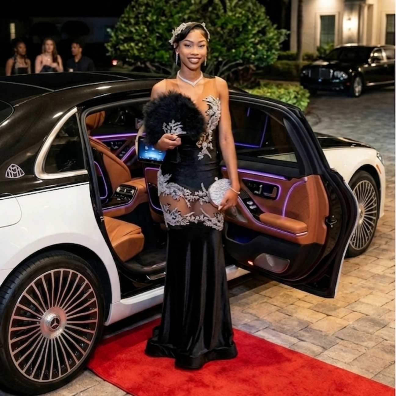A person in an elegant black dress with silver embroidery stands on a red carpet next to a luxury car with an open door.