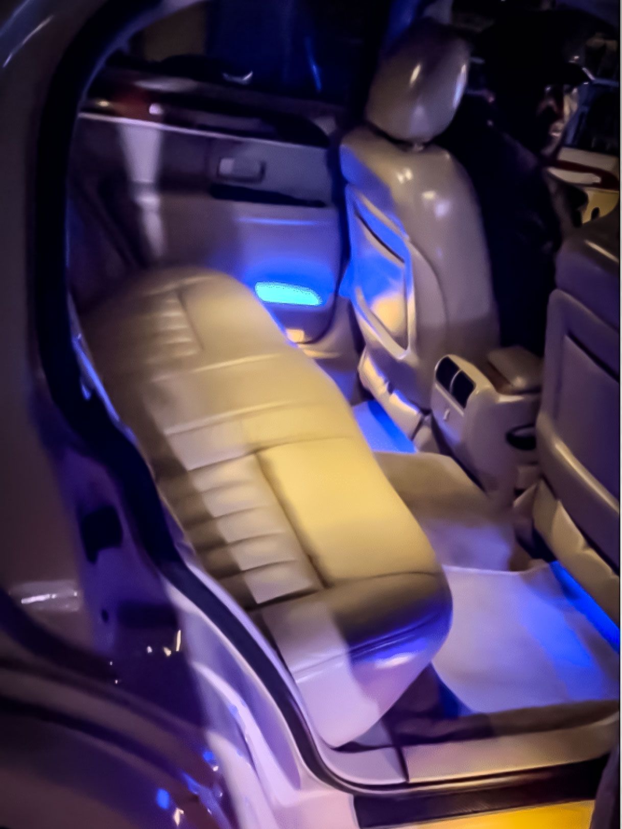 The rear interior of a car features grey leather seats and floorboards illuminated by vibrant blue ambient lighting.