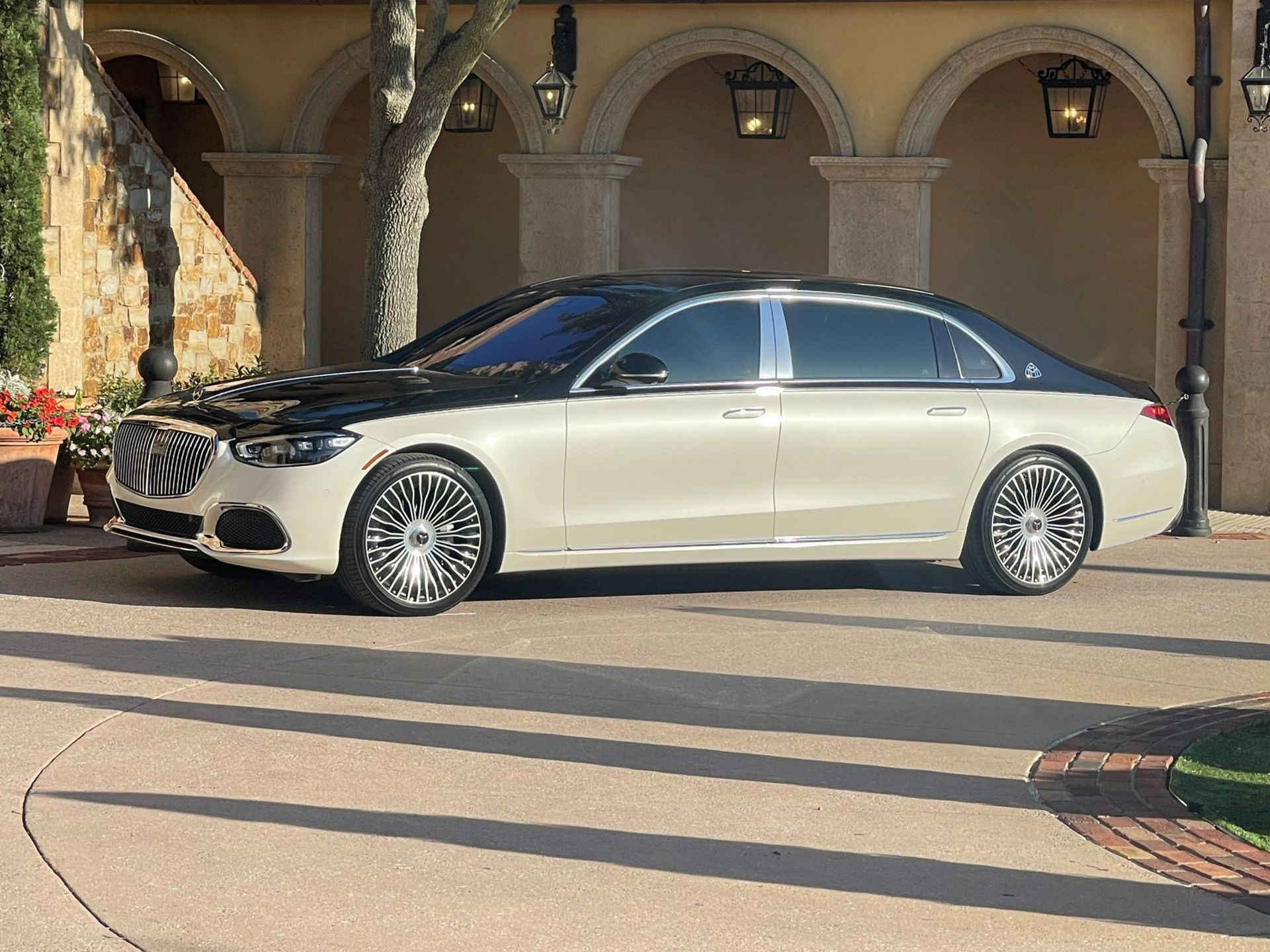 A two-tone black and white Mercedes-Maybach parked on a paved driveway in front of a building with arched entryways.