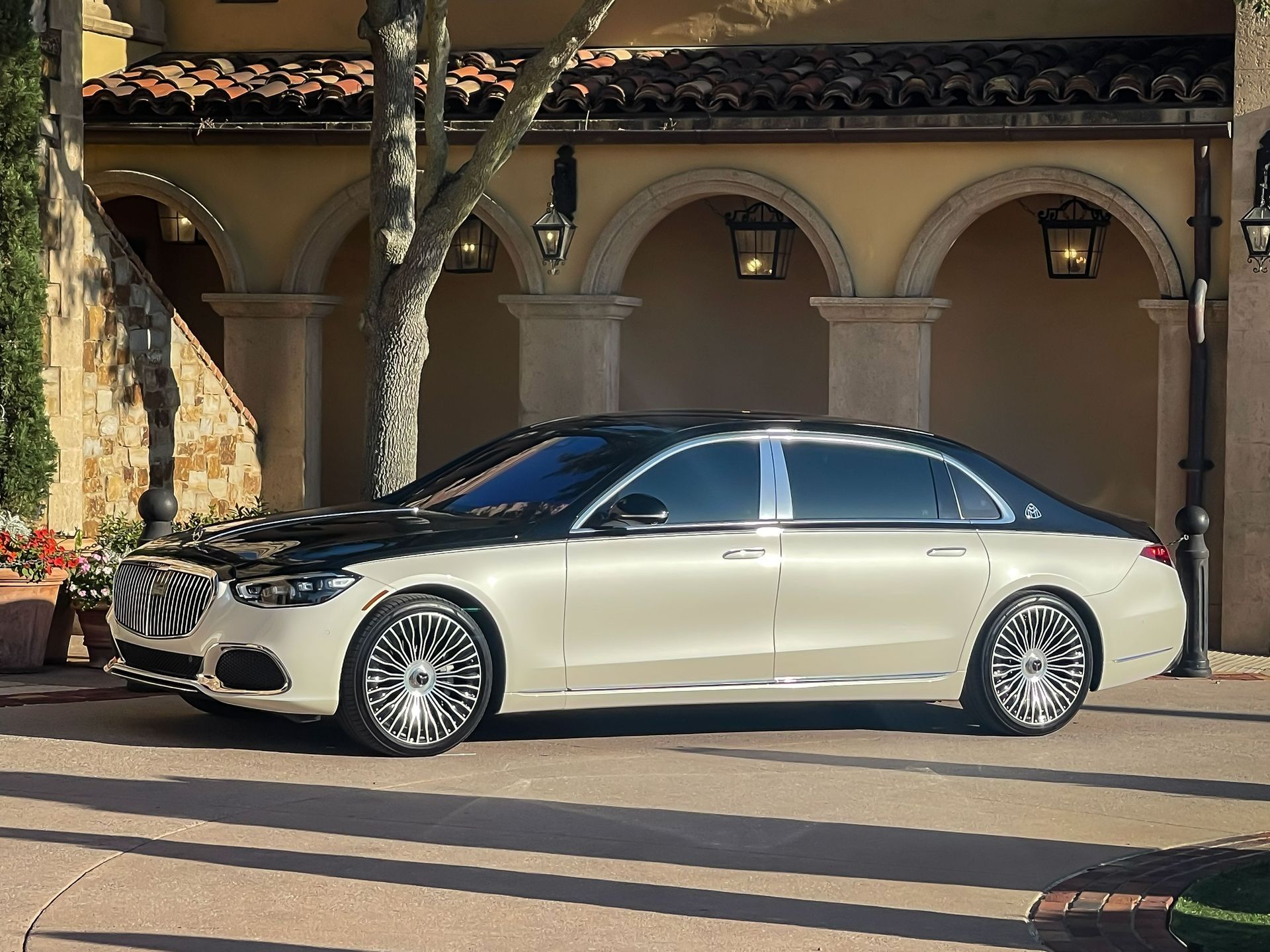 A two-tone black and cream Mercedes-Maybach parked outside a building with stone archways.