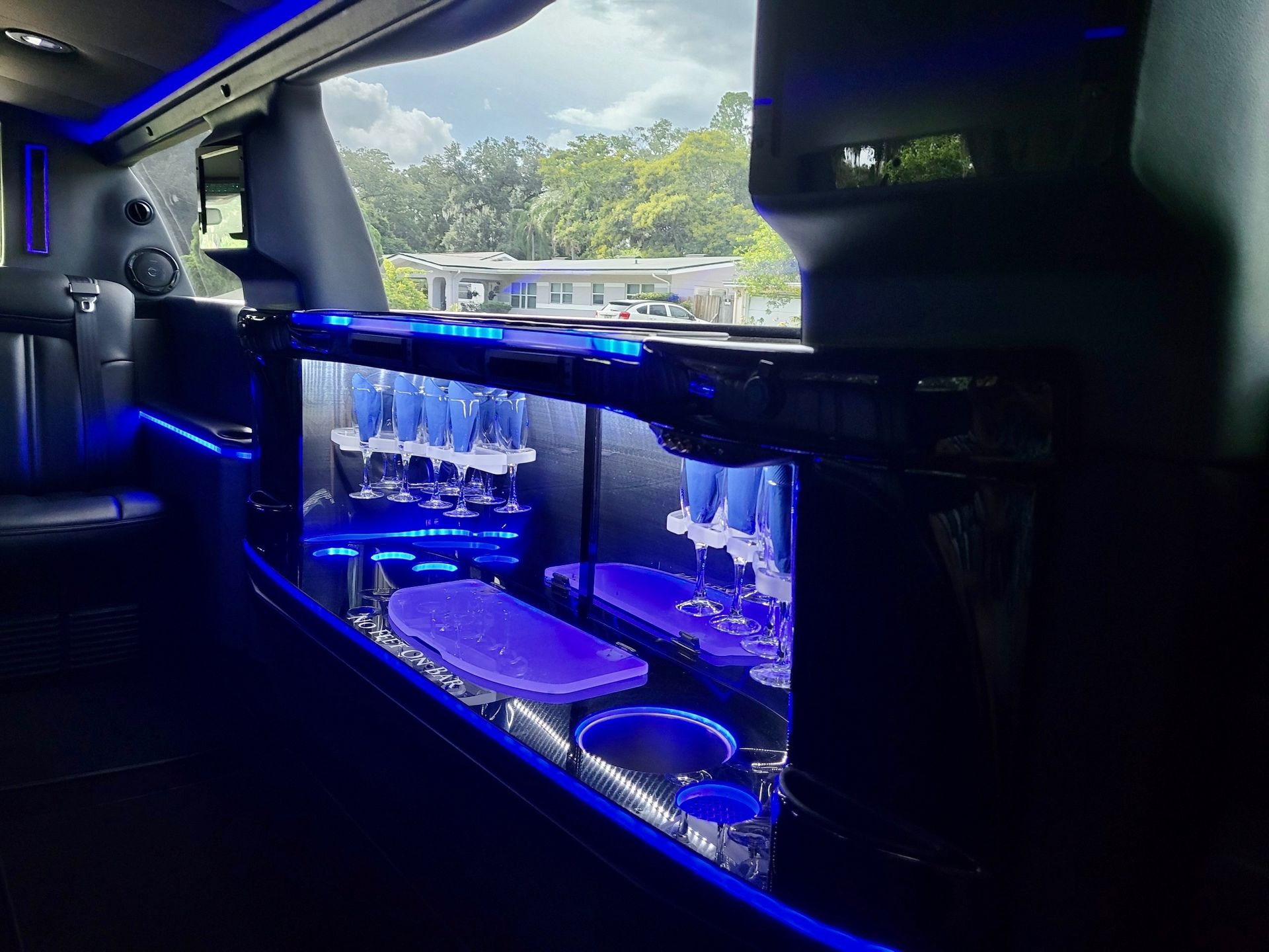 The interior of a limousine featuring a blue-lit bar area with glassware and seats, seen through a window.