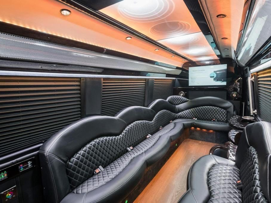 Interior of a luxury limo with black leather seating, wood floor, and a TV screen.