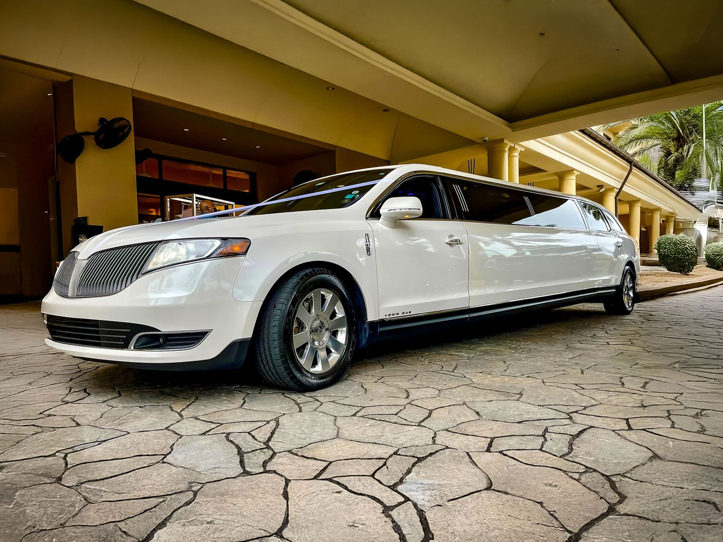 A white stretch limousine parked on a paved stone driveway in front of a building with columns.