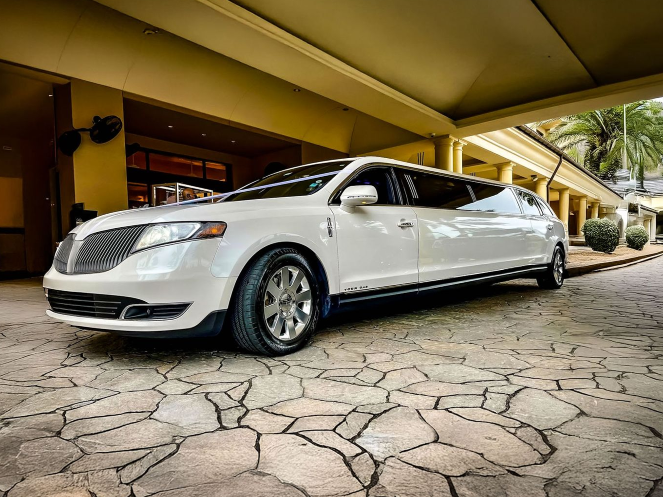 A white stretch limousine parked under a covered walkway on a stone-paved driveway.