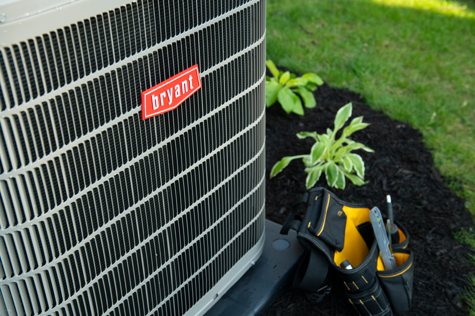 Bryant air conditioner next to gardening tools and a small plant on a lawn