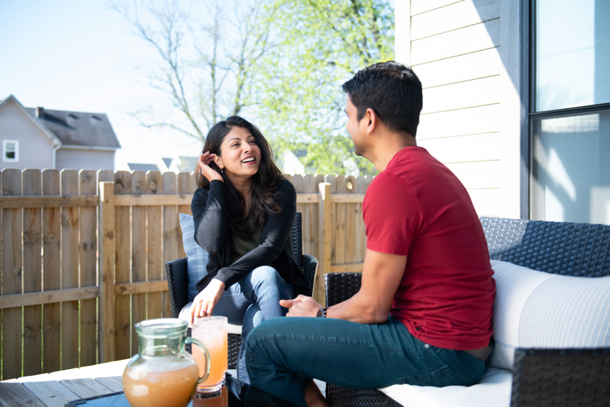 Two people talking on a patio, seated beside a small table with a candle and drinks.