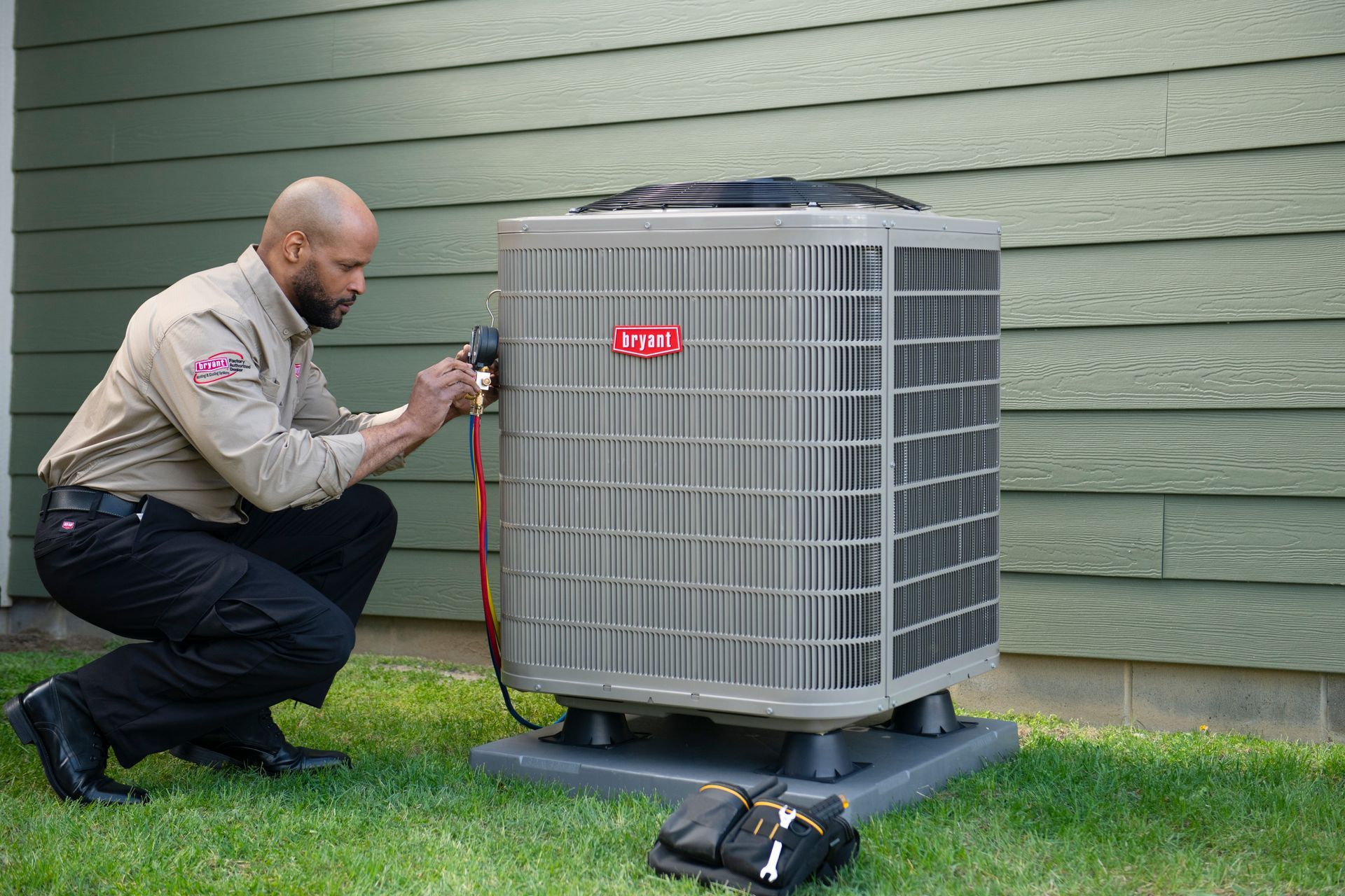 Technician inspecting an outdoor HVAC unit with gauges beside a house