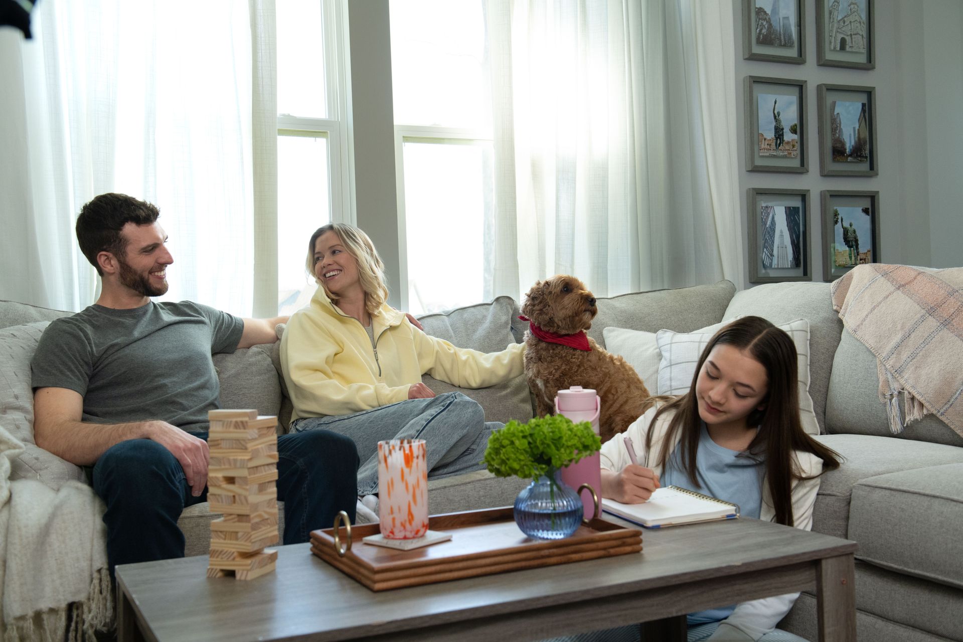 People relaxing in a bright living room, playing Jenga and drawing at a coffee table with a dog nearby.