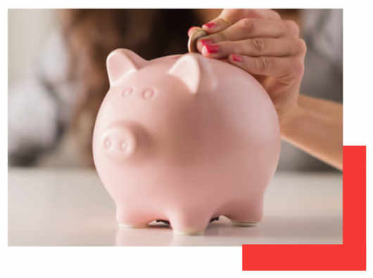 Hand placing a coin into a pink piggy bank on a white surface