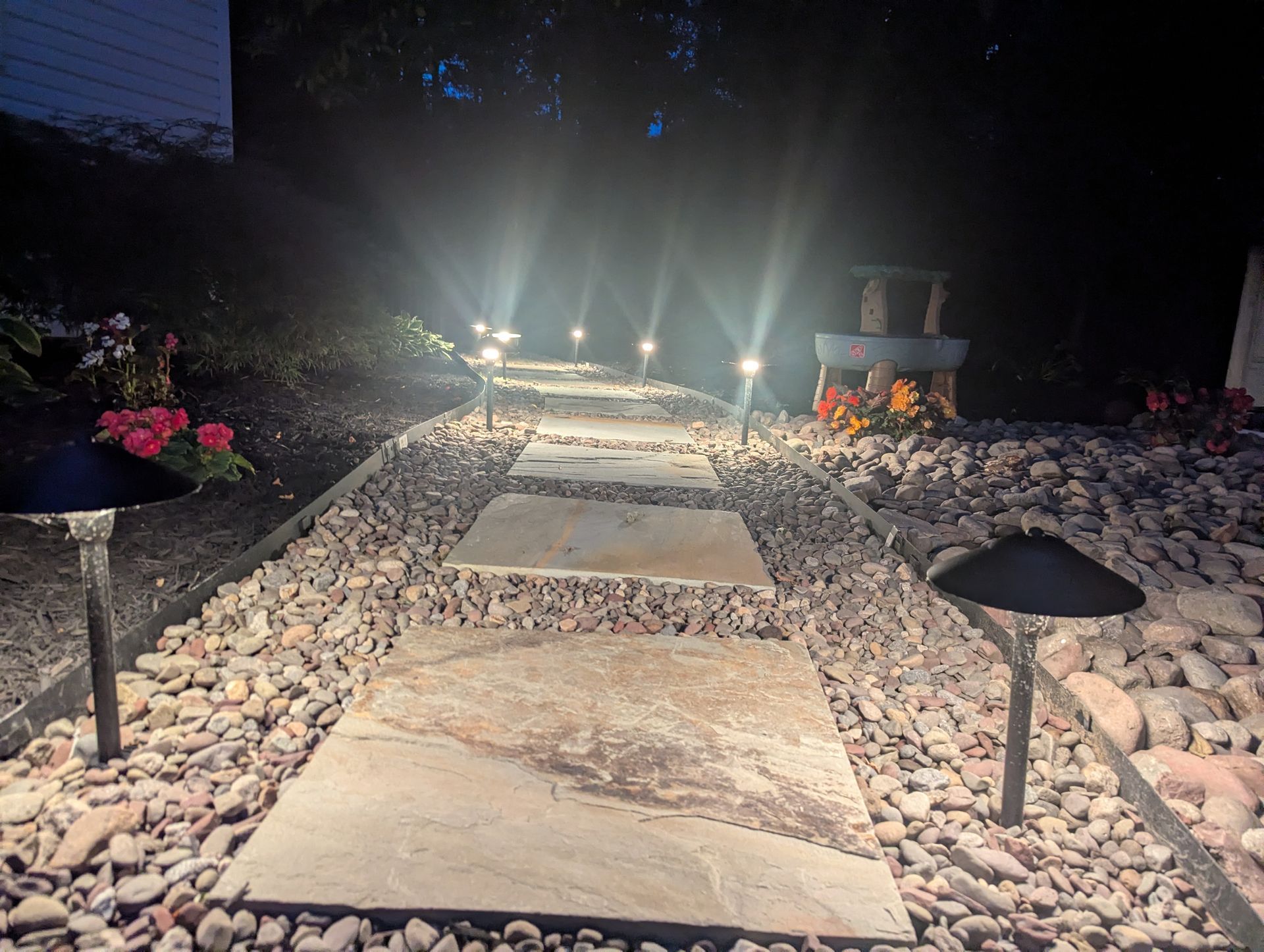 Landscaped garden bed with shrubs, mulch, and stone steps beside a gravel path