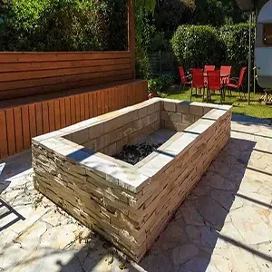 Backyard patio with a rectangular stone fire pit, wooden benches, and red flowers by a fence