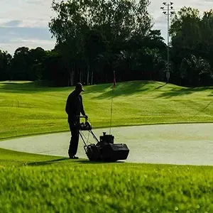 Person mowing grass near a pond on a sunny golf course