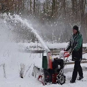Person using a snowblower to clear snow in a snowy yard, with snow spraying high into the air