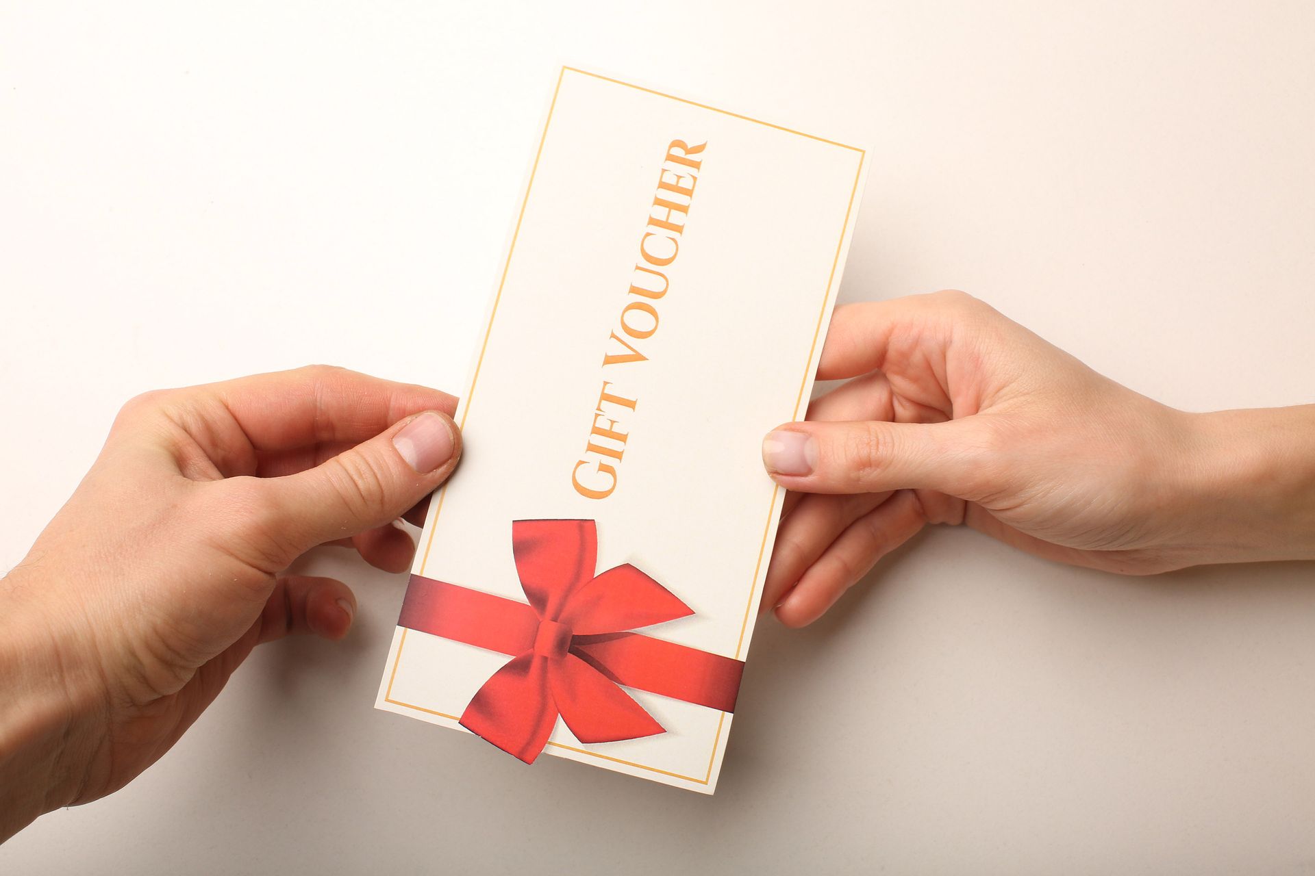 Hands holding a gift voucher tied with a red ribbon on a white background Hands holding a gift voucher tied with a red ribbon on a white background