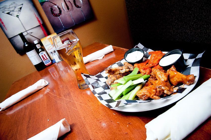 Restaurant table with a plate of wings, celery, dipping sauces, and a glass of beer