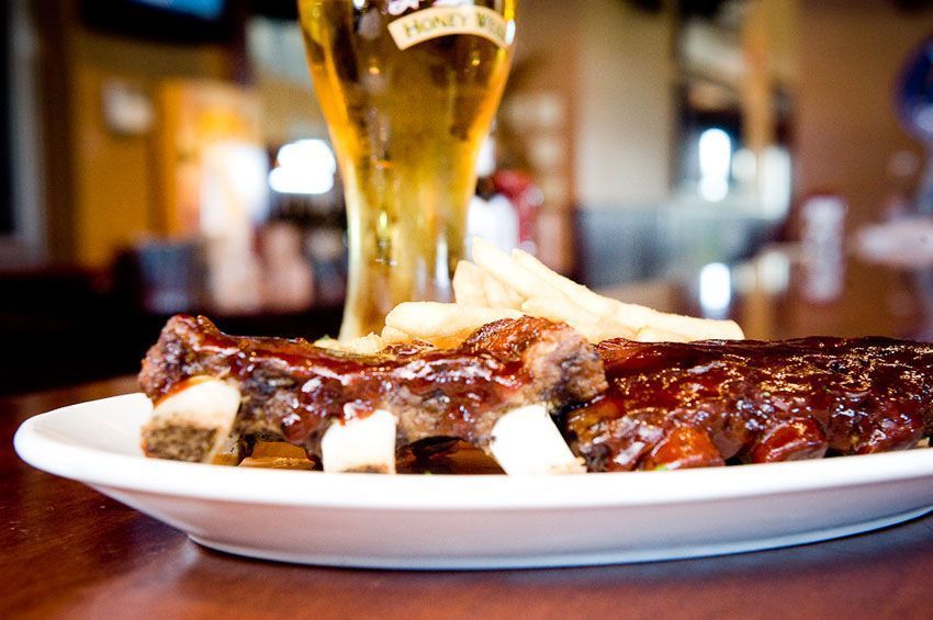 Barbecue ribs on a white plate with a beer glass in a warm restaurant setting